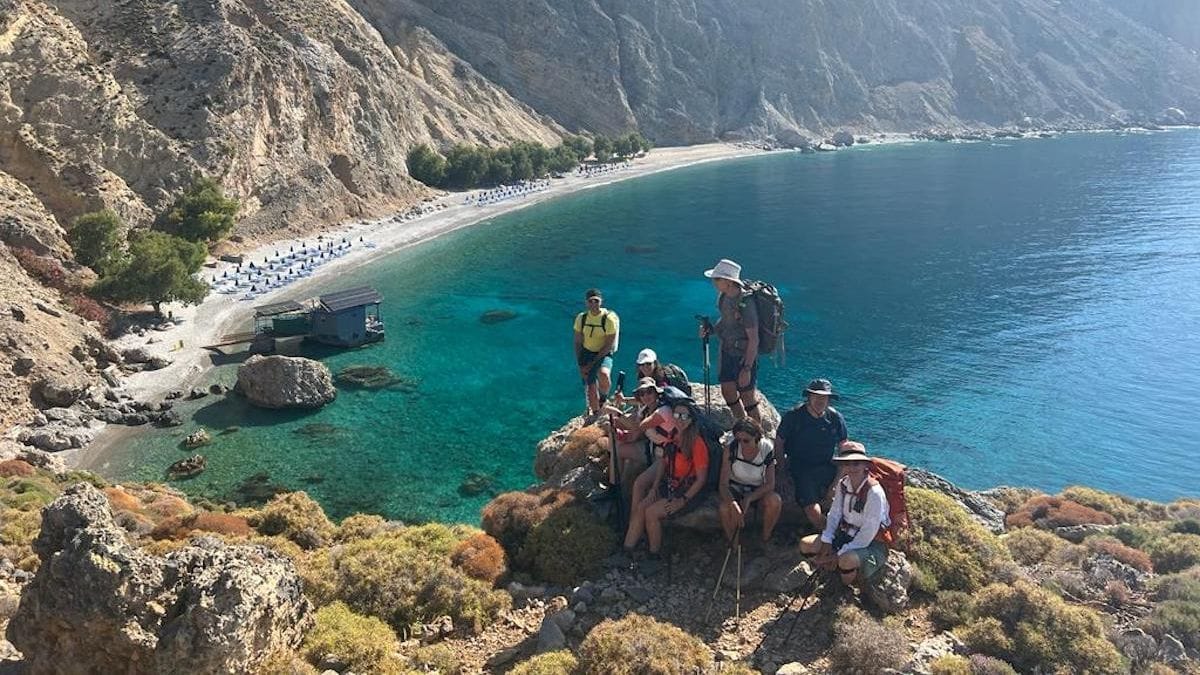 Hikers resting on a rocky coastal path above a turquoise bay
