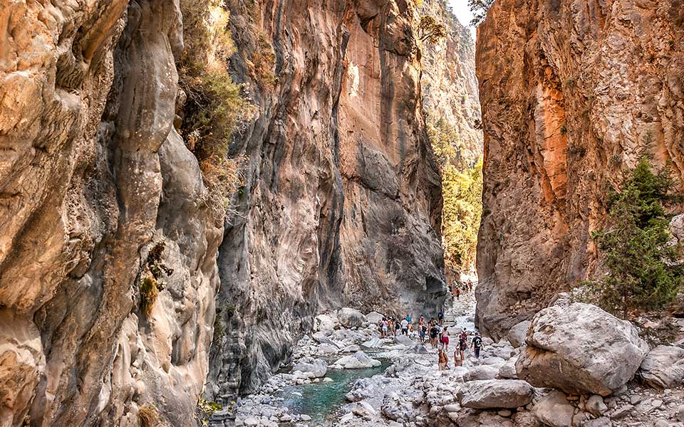 Walkers following a stream between tall rock walls in a Cretan gorge